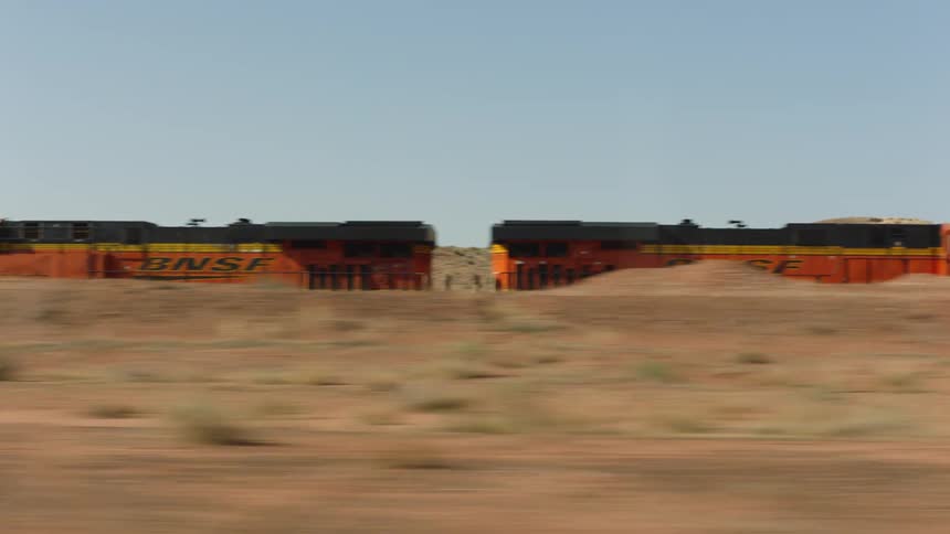 Train sits stalled next to road between mounds under a clear sky