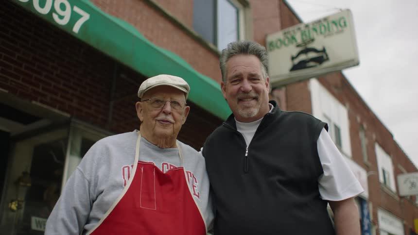 Father and son laugh while standing in front of a small town shop