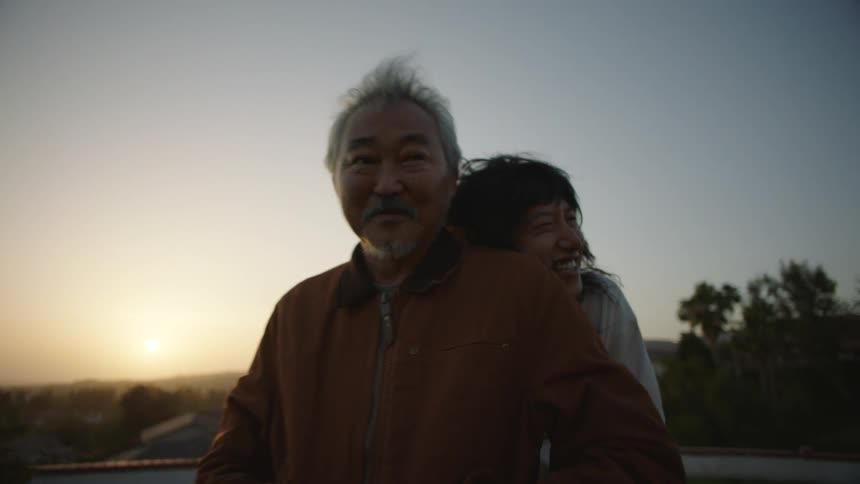 A man standing in the grass being hugged and leaned on by his adult son