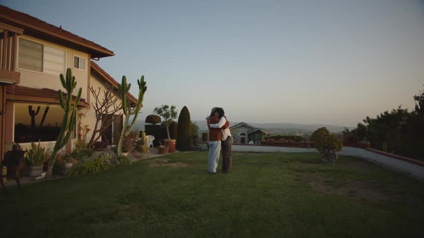 Two people standing on the grass in the backyard hugging at evening