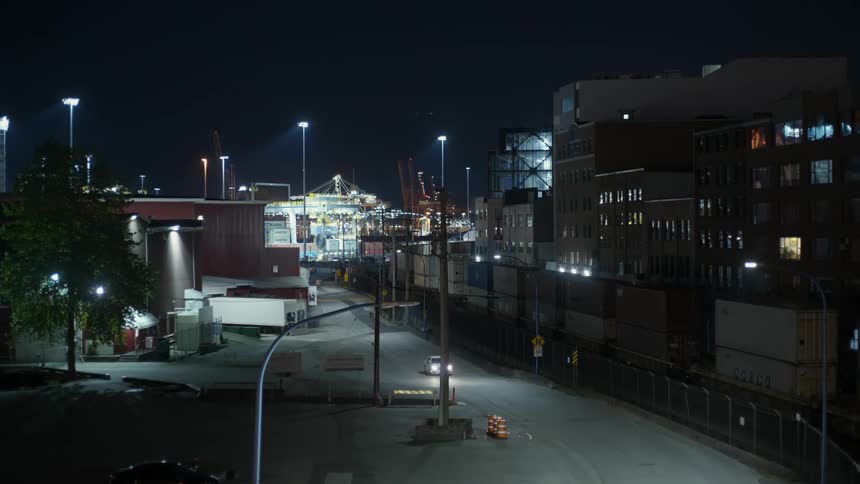 Vehicle driving on a road near a port filled with shipping containers at night