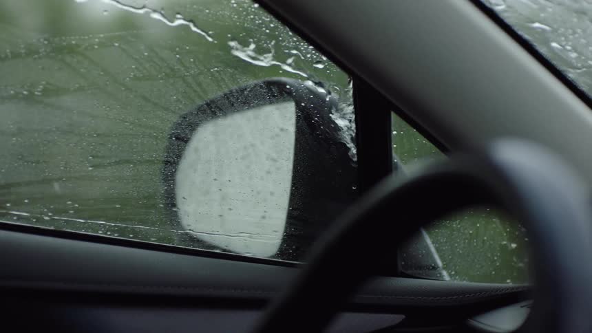 Water runs along the window and side mirror as car drives through the rain