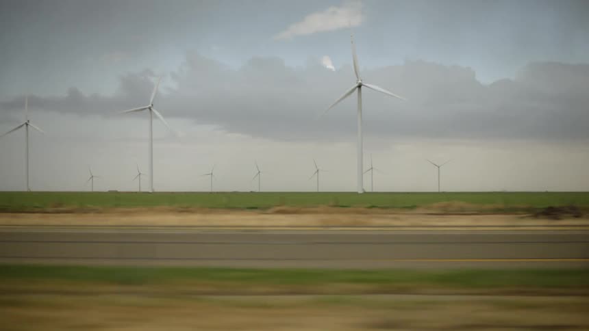 Traffic flows down highway past wind farm under a cloudy sky