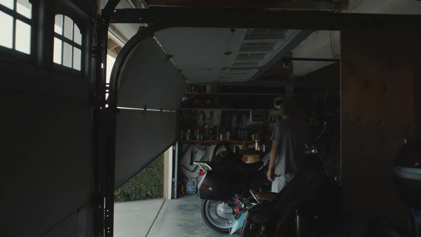 Older man and son walk around motorcycle as garage door is raised