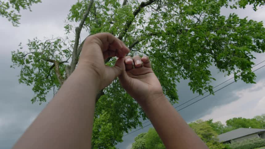 A person lays on the grass in the yard raising his hands to the sky