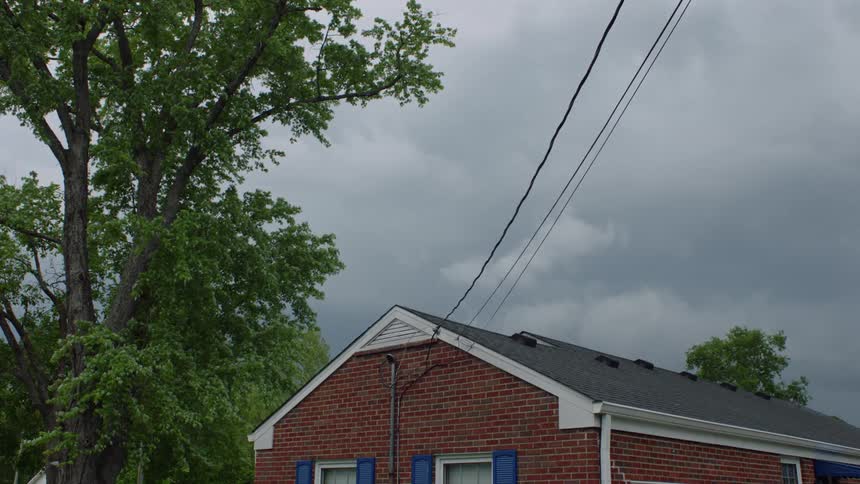 Power lines enter house near roof line under an overcast sky