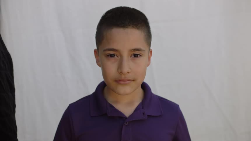 Young boy wearing blue shirt standing in front of white backdrop