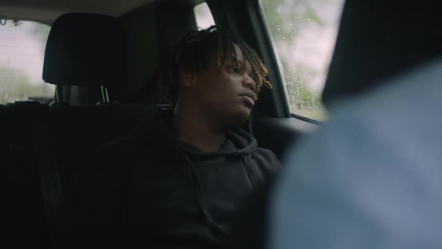 A teenage boy sitting in the backseat of a car looking out the window