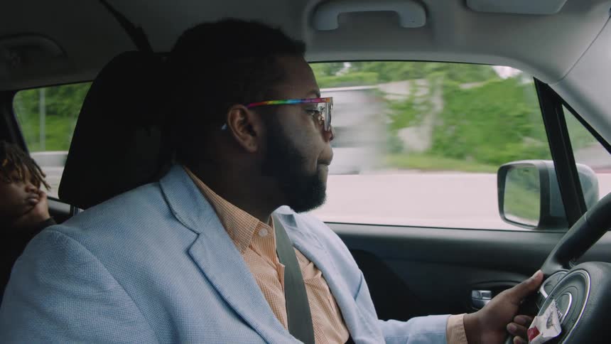 A man is driving an automobile with a boy in the back seat
