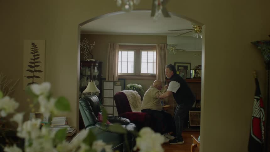 Older man greets then helps elderly man stand in a home