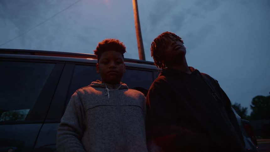 Two teenagers lean against the car