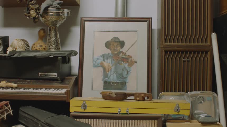 Picture of fiddle player sits near piano and instrument cases