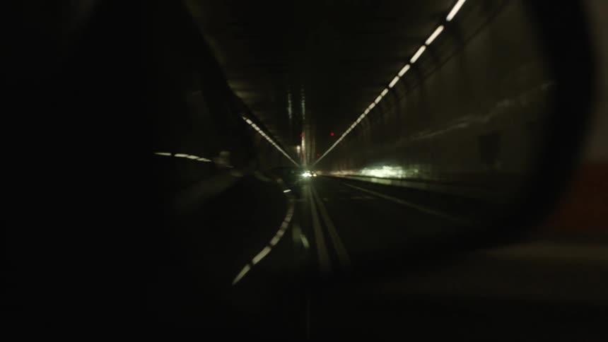 Side mirror reflects tunnel with several lines of lights