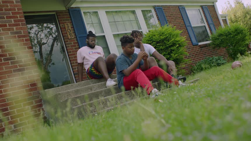 Three young men sit on the steps of the house