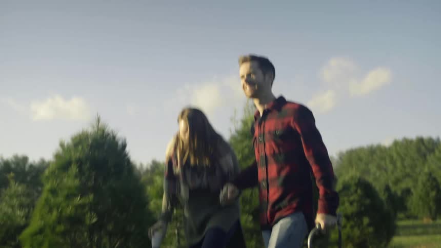 Man and woman hold hands as they walk near trees