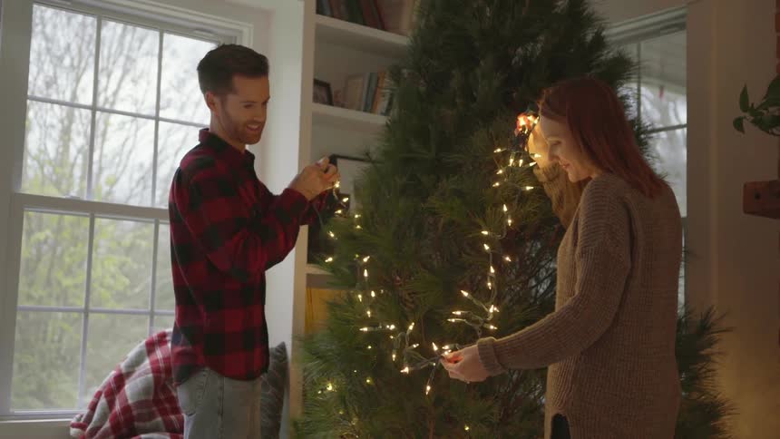 A couple are decorating a christmas tree with lights