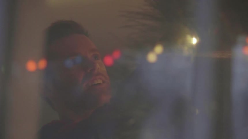 A man is applying christmas decorations to a tree