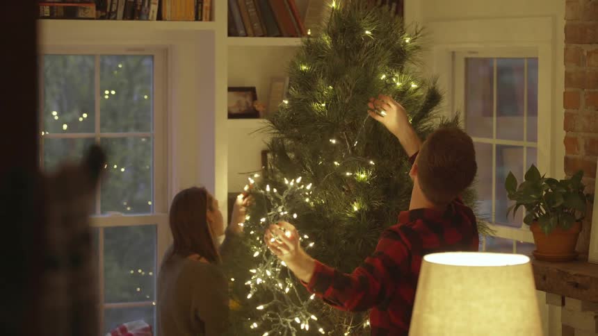 Man and woman put lights on a christmas tree
