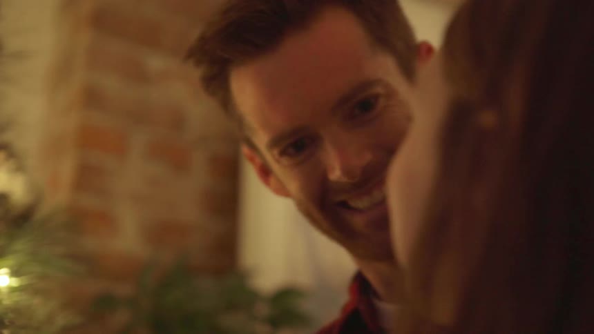 Couple smiling at each other as they decorate their christmas tree
