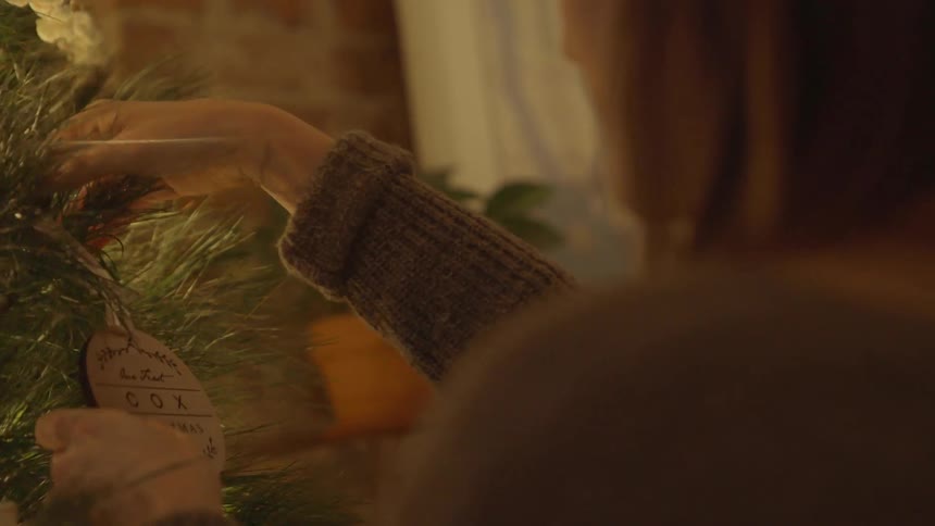 A woman is putting on a christmas ornament to the tree