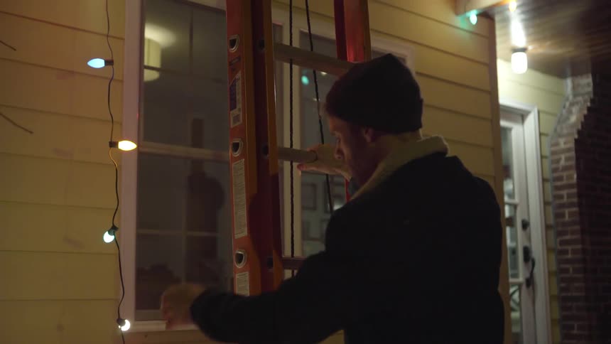 A man hangs christmas lights on a house