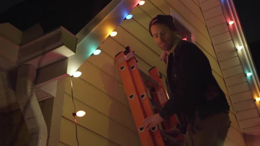 A man is finishing attaching lights to the roof of the house