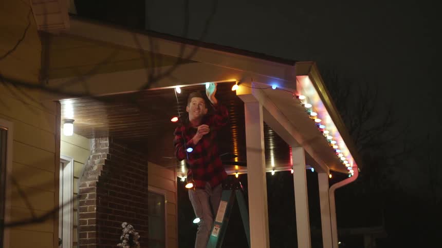 A man hangs christmas lights on a house