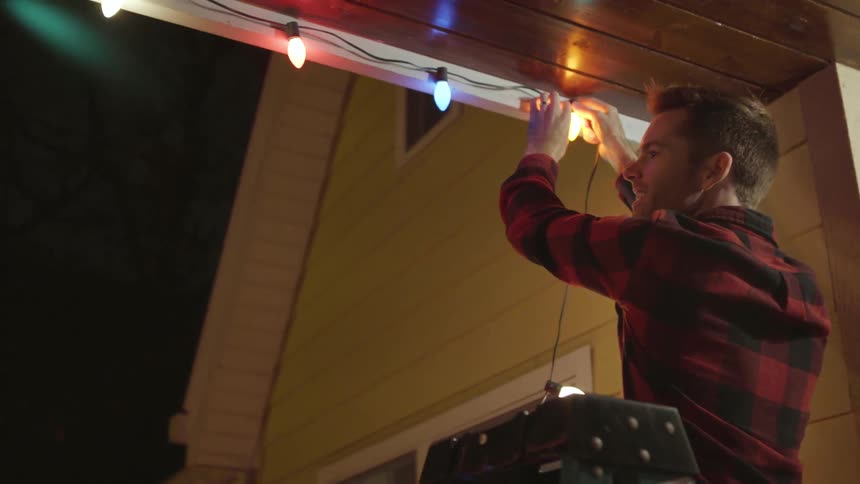 A man hangs christmas lights on a house