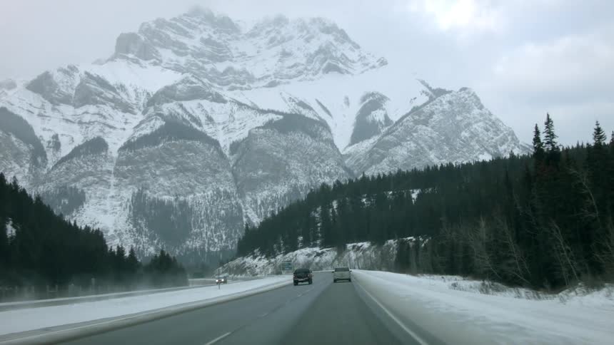 Vehicles moving on a highway towards the snow covered mountain