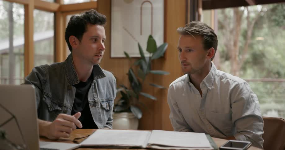 Two men talk while looking at a laptop