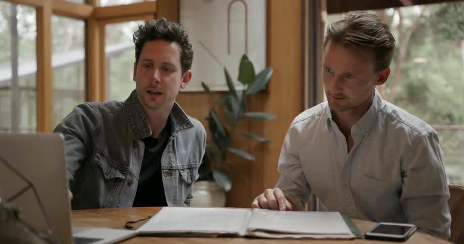 Two men are looking at a laptop, one of the men is explaining something to the other