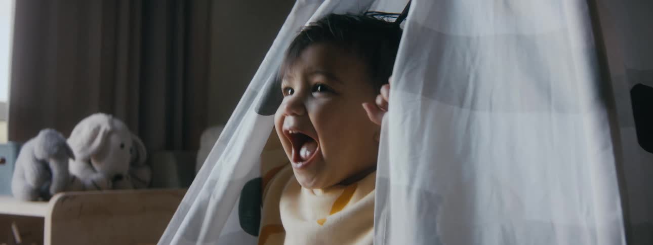 Young child smiles while looking through open flap of tent