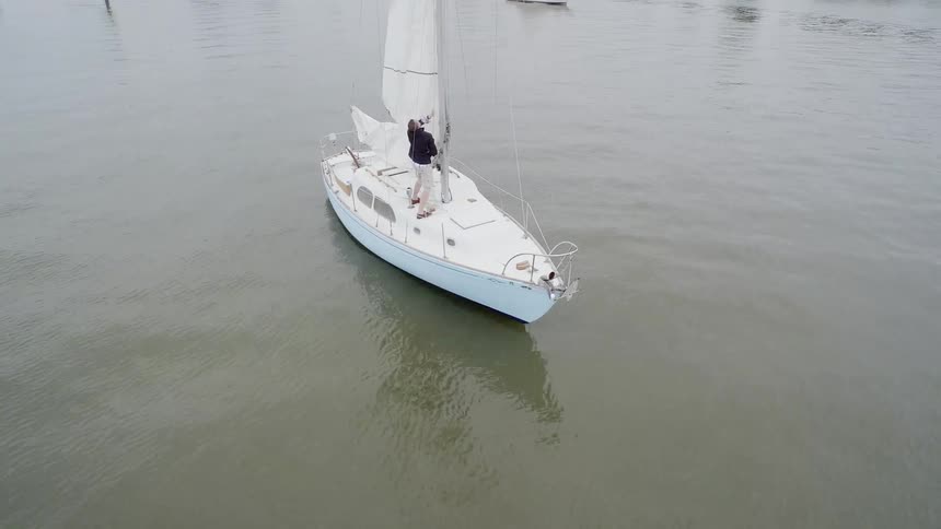 A man lifts a white sail on his sailboat
