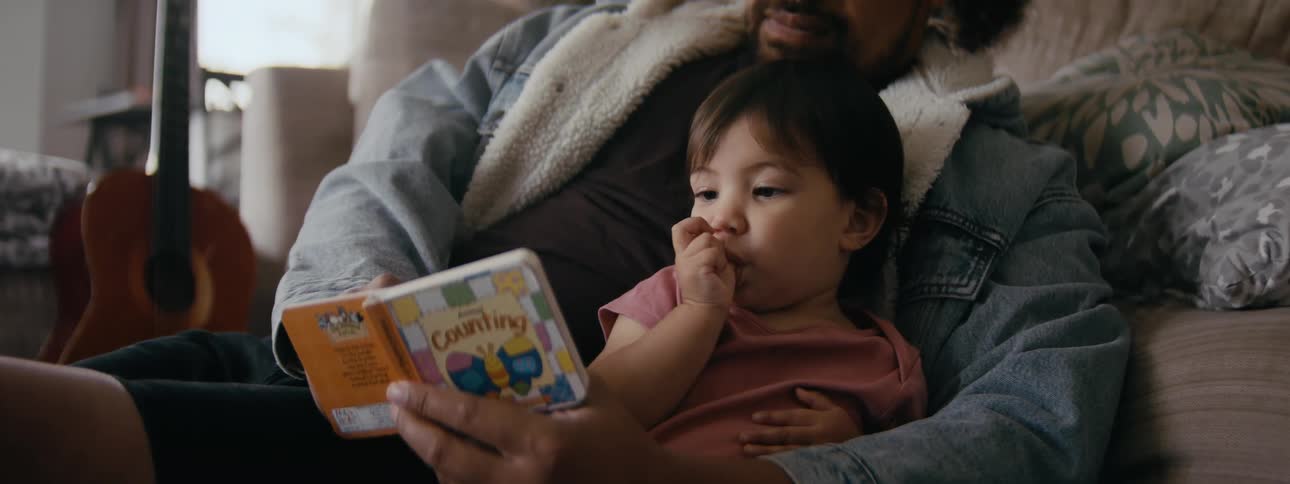 Small child sitting on fathers lap while he reads a picture book