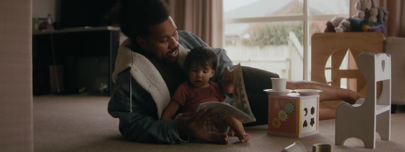 Dad lying on the rug reading to his little girl
