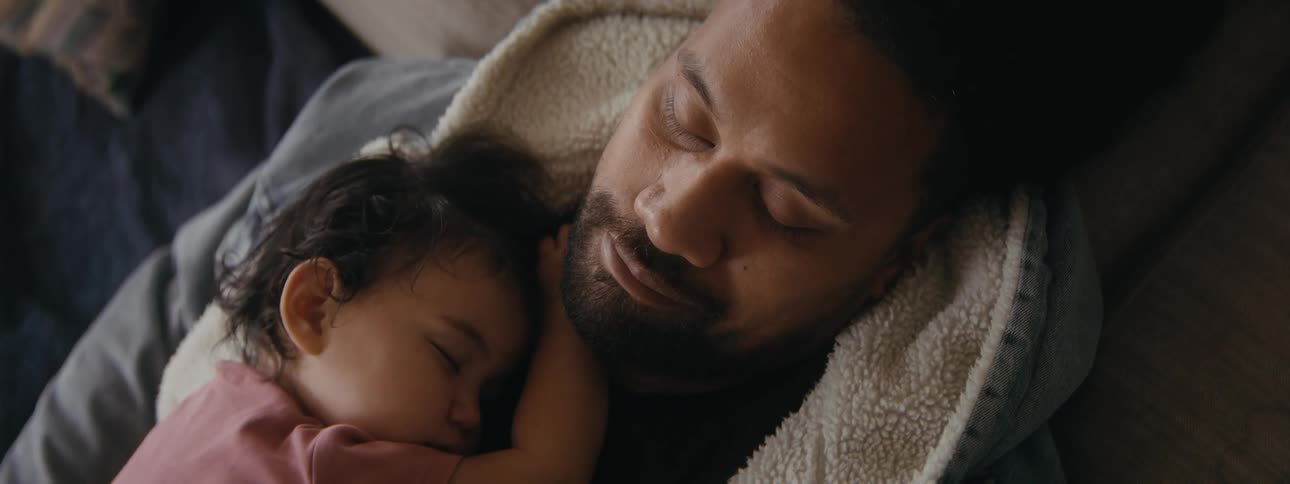 A man is sleeping with his baby sleeping on his chest
