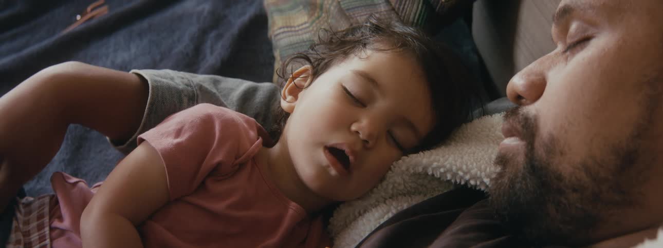 A baby sleeps as a father holds in him a bed and looks at him