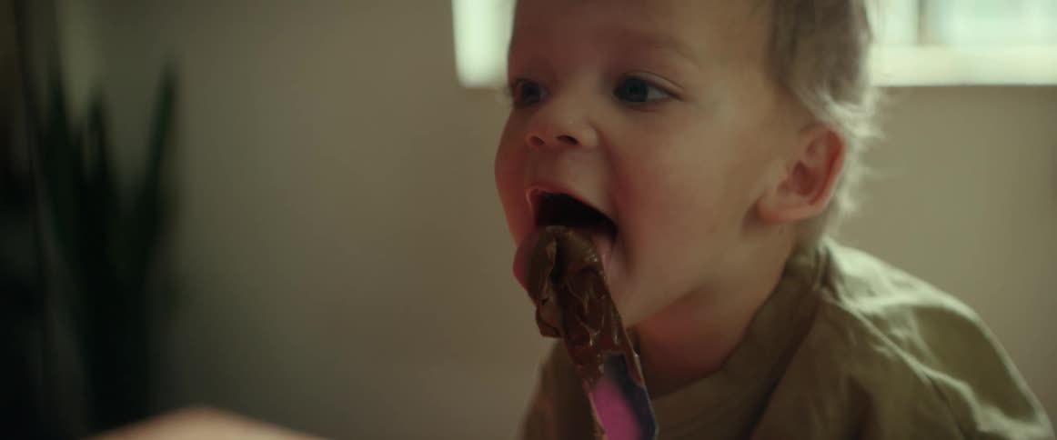 A little boy smiles as he licks chocolate on a spatula