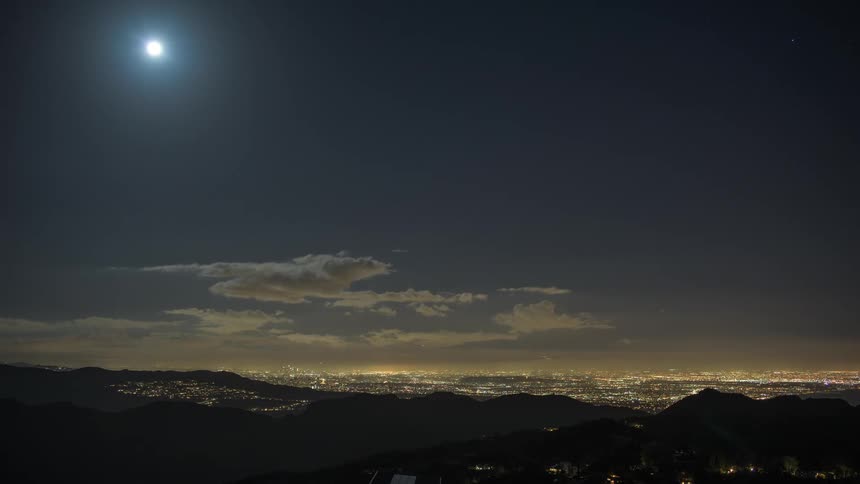 The moon is high in the sky over the hills looking down on a city