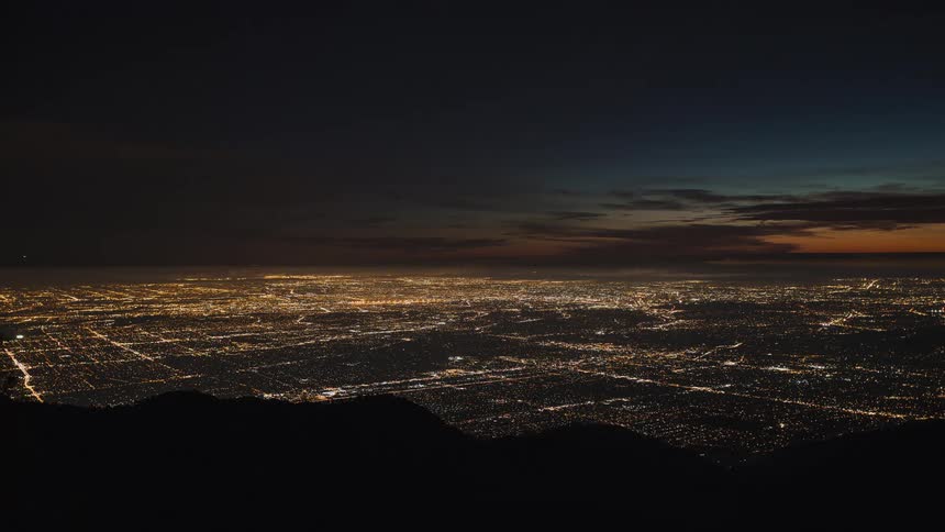 Clouds move across and the sun sets over a city grid shimmering at night