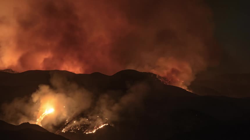 Sparks burst into flames as a raging fire burns behind a hill blowing smoke into the air