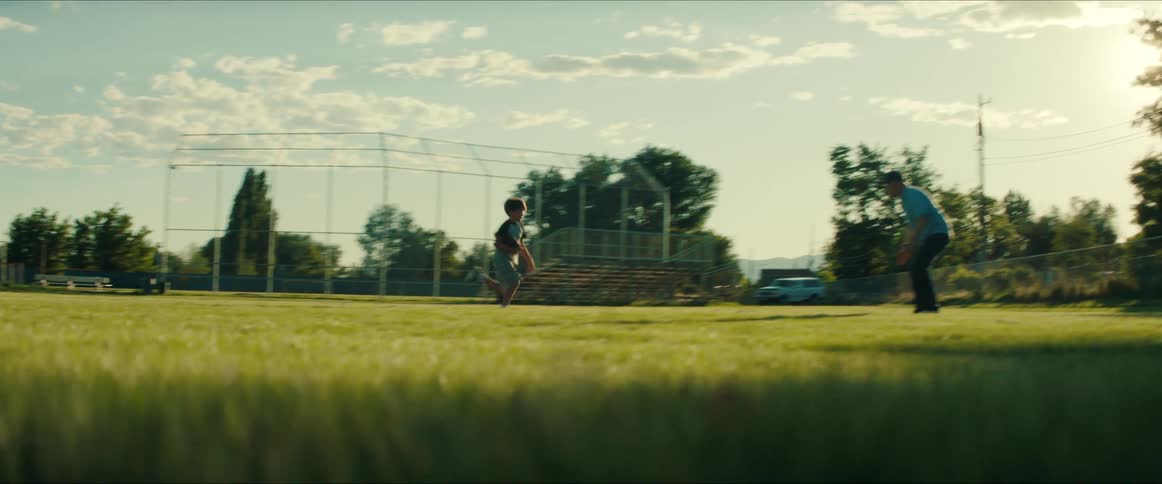 A father and son are playing football on a grass field in a park