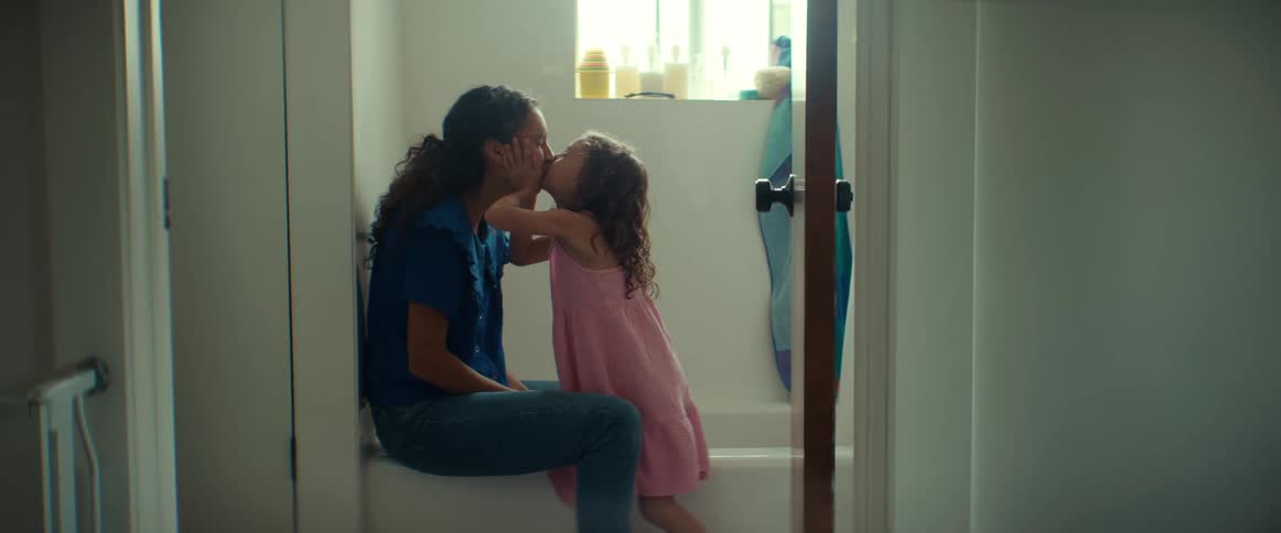 A young girl gives a spontaneous kiss to a woman during a sweet, everyday moment at home