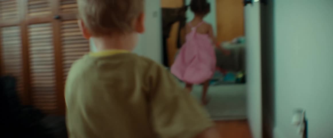 A little boy chases a little girl into a bedroom where she playfully jumps onto the bed