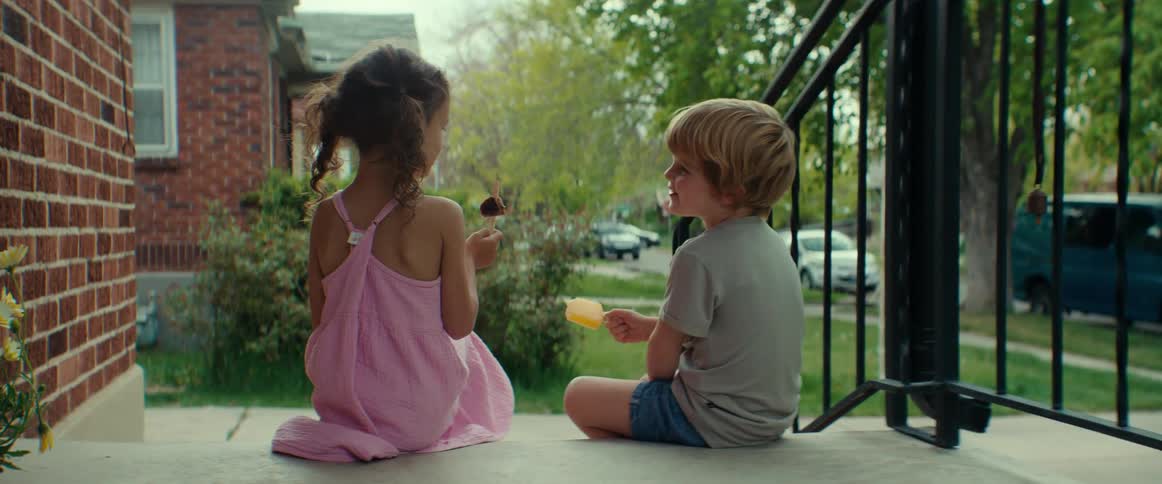 A boy and girl sitting side by side on the porch steps eating popsicles