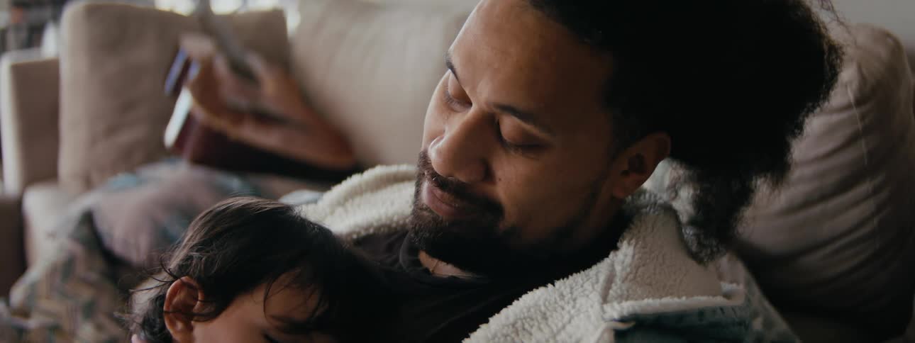 A man holds a small child resting against his chest while sitting indoors during the day