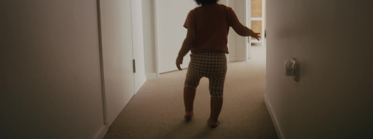 Child toddles down hallway passing doll