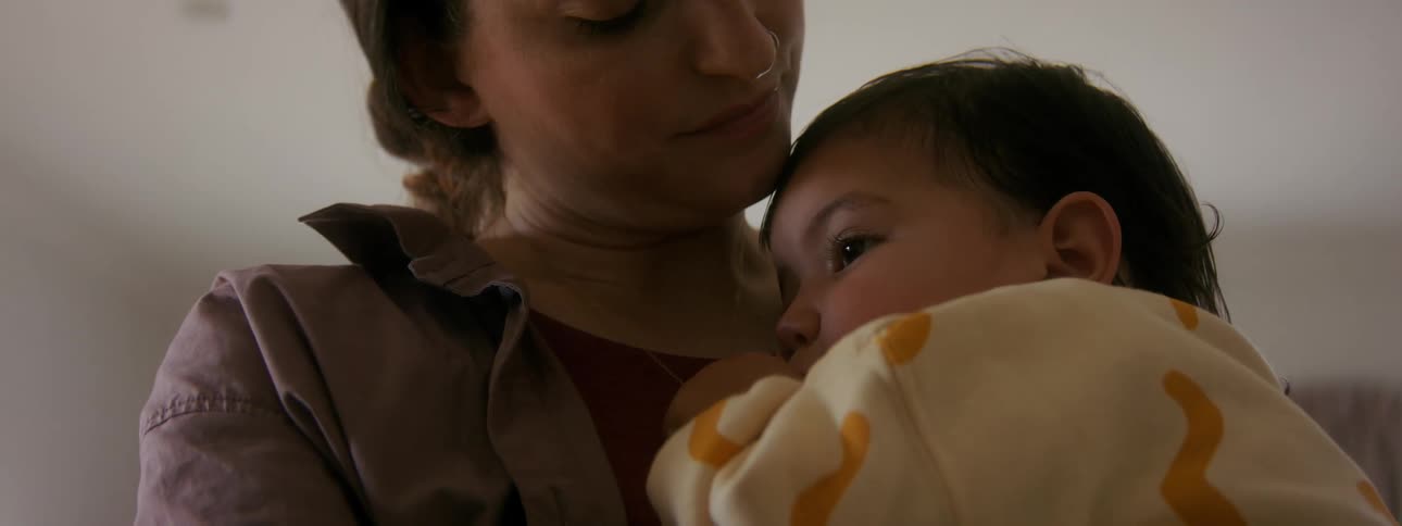 Child sucks thumb while being held by mother