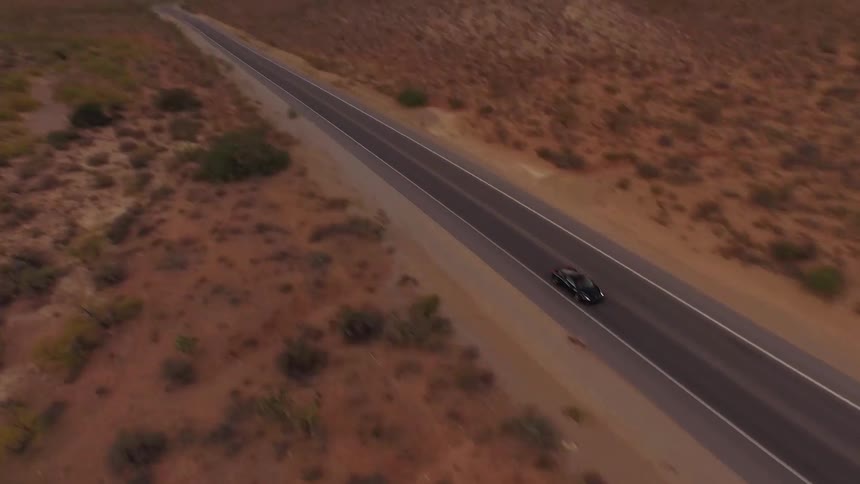 A car races down a road surrounded by a desert
