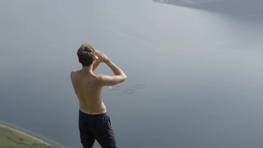Active male hiker shouting from a rugged mountain peak overlooking a vast wilderness landscape.